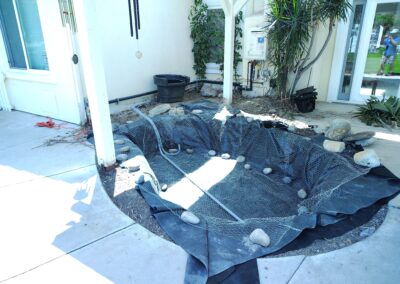 Pond construction site with protective mesh, landscaping stones, and garden equipment visible.