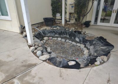 Landscape pond area with rocks, fabric liner, and surrounding concrete patio for outdoor design.