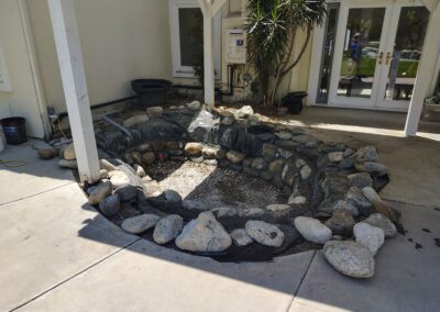 Outdoor pond area under construction with rocks and mesh around a gravel base.