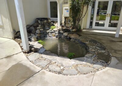 Peaceful backyard pond with rocks and greenery, surrounded by a stone pathway.