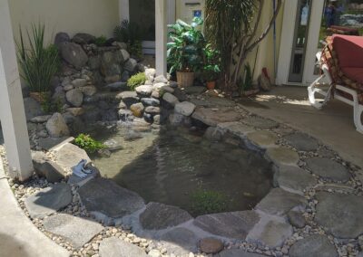 Tranquil garden pond with rocks, plants, waterfall, and seating area for relaxation.